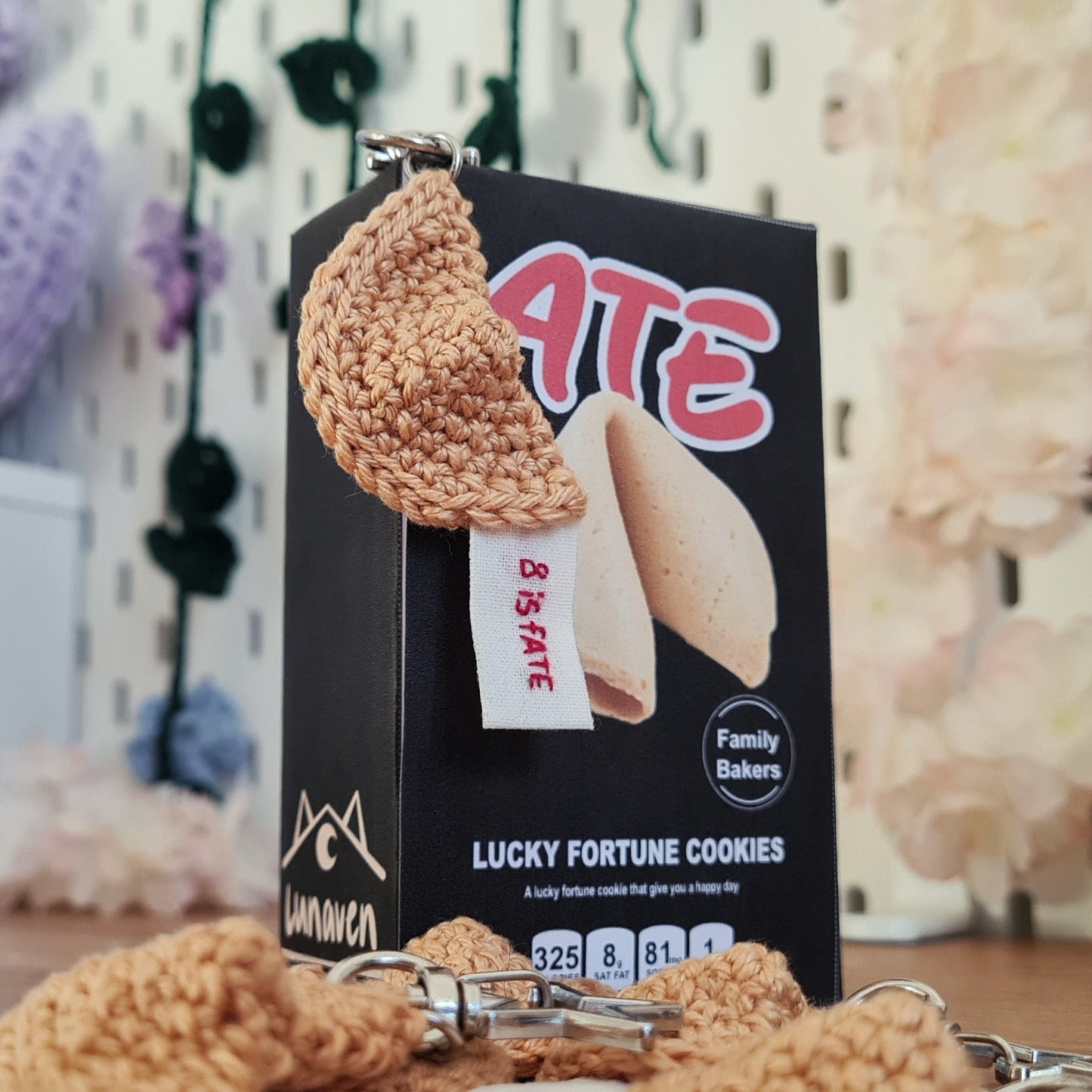 Porte-clés en crochet avec message brodé à la main, inspiré de l'album ATE de Stray Kids. Le fortune cookie est beige, le message est brodé en rouge sur tissu blanc cassé, on peut le voir dépasser du biscuit. Il est écrit 8 is fate. Le porte-clés est posé sur une boîte de fortune cookie ATE. Le mousqueton est en forme d'étoile.