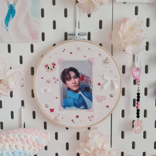 Cadre-photo ou pc-holder, cette broderie offre un encadrement girly et original. Dans un style coquette, habillez votre photocard ou polaroid favori. Sur la photo, la pc au centre représente Changbin du groupe Stray Kids. Autour de la pc il y a différents éléments brodés en rose et beige : un ourson avec des noeuds, des coeurs, des fleurs, une tasse à thé, une lettre. D'autres éléments en 3D viennent rehausser la broderie : des perles, strass et rubans. Le tout est encadré dans un cercle à broder.